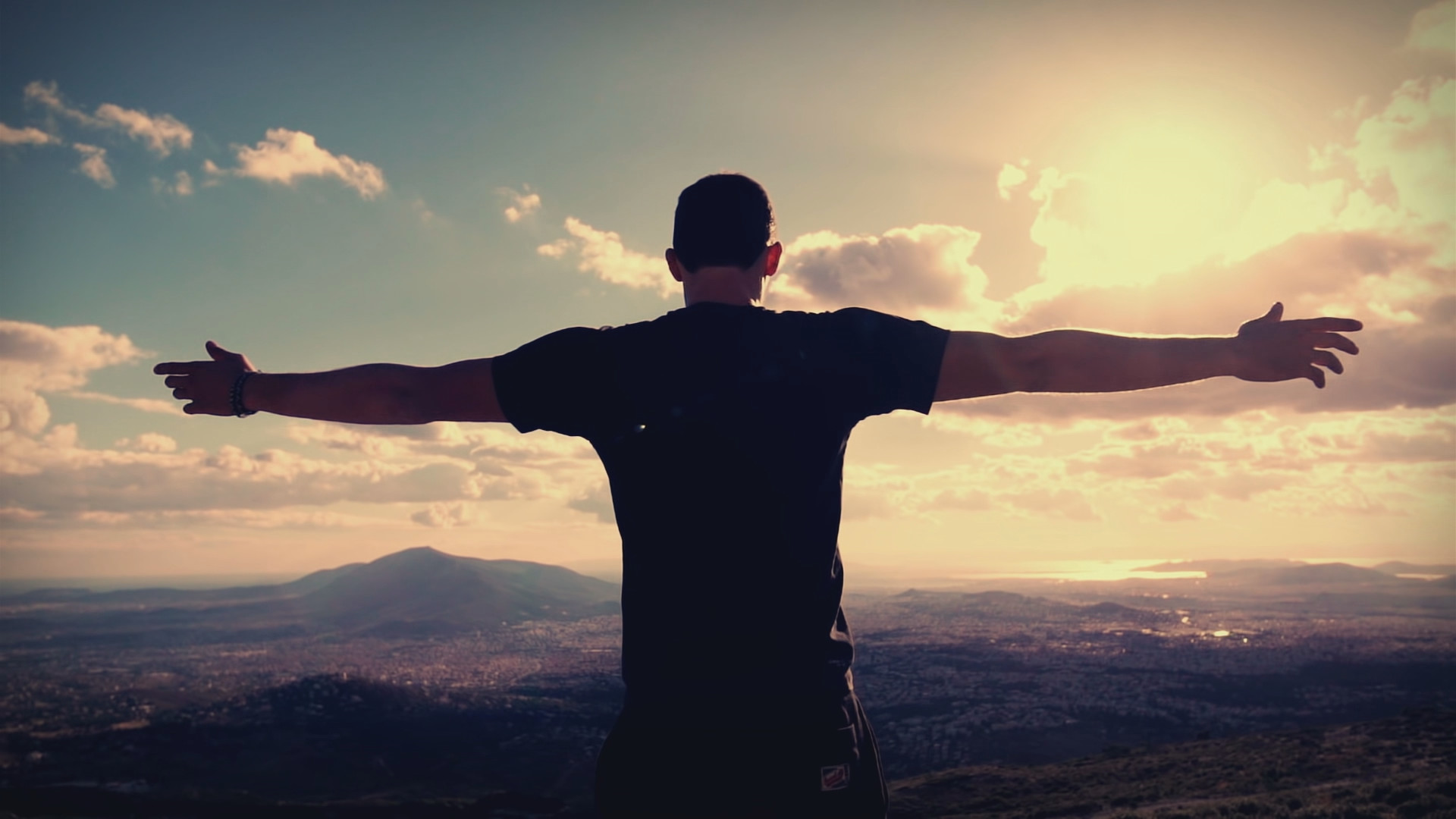 Man standing on a mountain with his arms outstretched looking at the landscape with us.