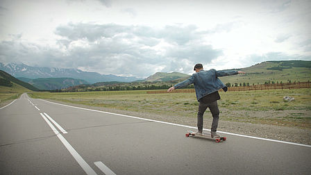 Man on a street with skateboard, mountains in the background.