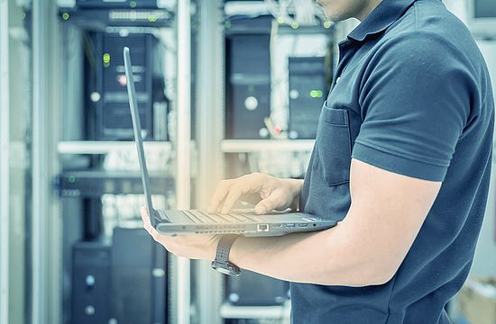 Man standing with open notebook in front of server cabinet.